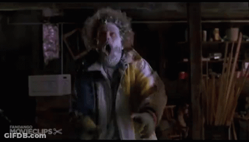 A Man In A Yellow Jacket With A Mask On His Face Is Standing In A Room . GIF