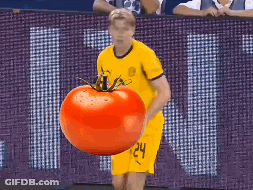 A Man In A Yellow Jersey Is Holding A Large Tomato In Front Of A Sign That Says Ucl GIF