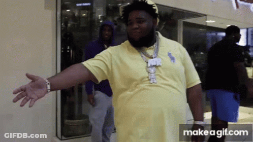 A Man In A Yellow Polo Shirt Is Standing In Front Of A Store Window With His Arms Outstretched . GIF