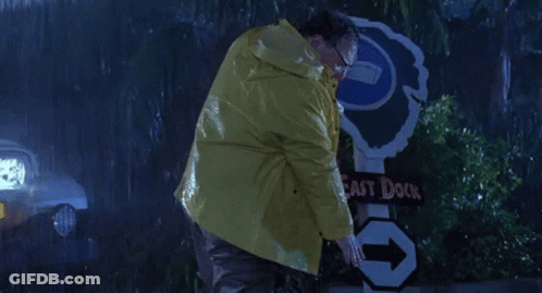A Man In A Yellow Raincoat Is Standing Next To A Sign That Says East Dock GIF