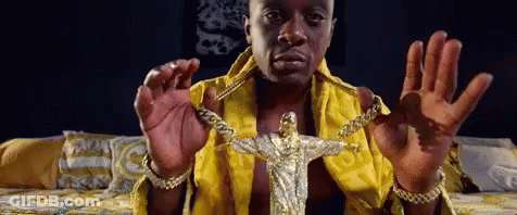 A Man In A Yellow Robe Is Holding A Gold Jesus Pendant GIF