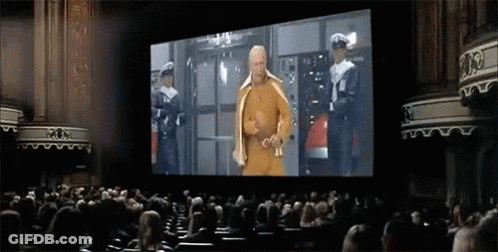 A Man In A Yellow Robe Is Standing In Front Of A Large Screen In An Auditorium .. GIF
