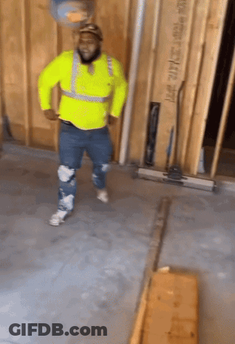 A Man In A Yellow Safety Vest Is Dancing In A Room With A Wall That Says Lmt 2014 On It GIF