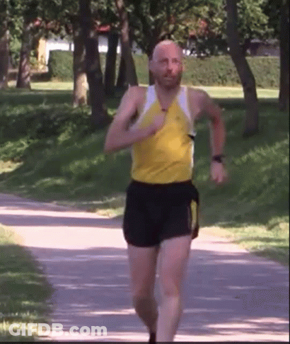 A Man In A Yellow Shirt And Black Shorts Is Running Down A Path GIF