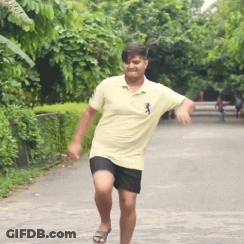 A Man In A Yellow Shirt And Black Shorts Is Running Down The Street GIF