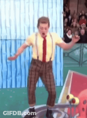 A Man In A Yellow Shirt And Brown Pants Is Standing On A Platform GIF