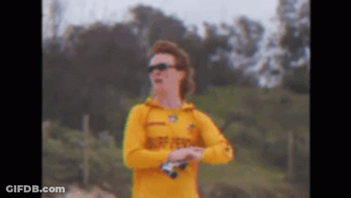 A Man In A Yellow Shirt And Sunglasses Is Standing On A Beach Holding Binoculars . GIF