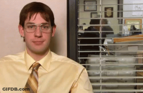 A Man In A Yellow Shirt And Tie Is Standing In Front Of A Window With Blinds . GIF
