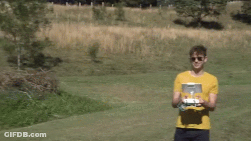 A Man In A Yellow Shirt Holds A Remote Control In His Hands GIF