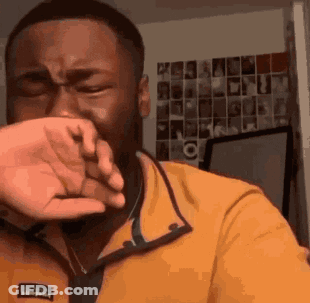 A Man In A Yellow Shirt Is Covering His Face With His Hand . GIF