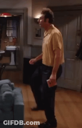 A Man In A Yellow Shirt Is Dancing In A Living Room With A Blue Couch . GIF