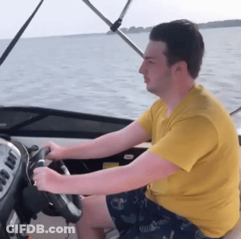 A Man In A Yellow Shirt Is Driving A Boat In The Ocean GIF