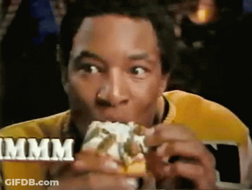 A Man In A Yellow Shirt Is Eating A Hamburger With The Word Mmmm In The Background GIF