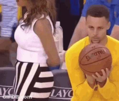 A Man In A Yellow Shirt Is Holding A Basketball In His Hands While A Woman Stands Behind Him . GIF