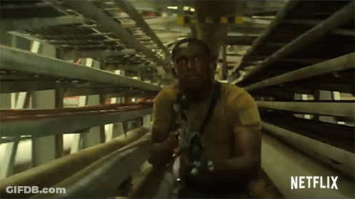 A Man In A Yellow Shirt Is Holding A Gun In A Tunnel With Netflix Written On The Bottom GIF