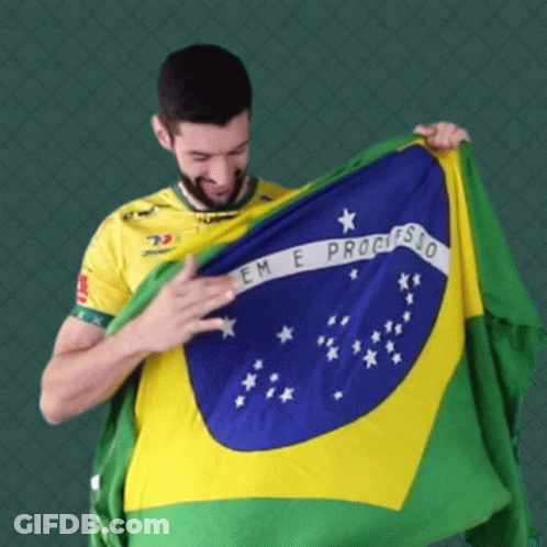 A Man In A Yellow Shirt Is Holding Up A Flag That Says Em E Progresso GIF