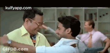 A Man In A Yellow Shirt Is Hugging Another Man In A Room . GIF