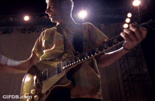 A Man In A Yellow Shirt Is Playing A Guitar In A Dark Room GIF