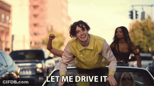 A Man In A Yellow Shirt Is Riding In The Back Of A Car With The Words Let Me Drive It Written Below Him . GIF