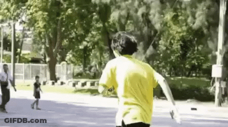 A Man In A Yellow Shirt Is Running Down A Street In A Park . GIF