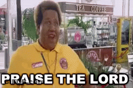 A Man In A Yellow Shirt Is Saying `` Praise The Lord '' In Front Of A Tea Coffee Stand . GIF