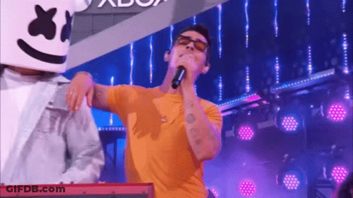 A Man In A Yellow Shirt Is Singing Into A Microphone While A Man In A White Jacket Is Playing A Keyboard . GIF