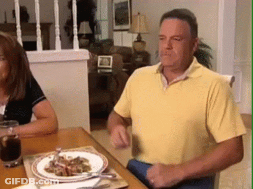 A Man In A Yellow Shirt Is Sitting At A Table With Plates Of Food On It GIF