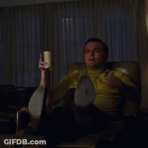 A Man In A Yellow Shirt Is Sitting In A Chair Pointing At Something GIF