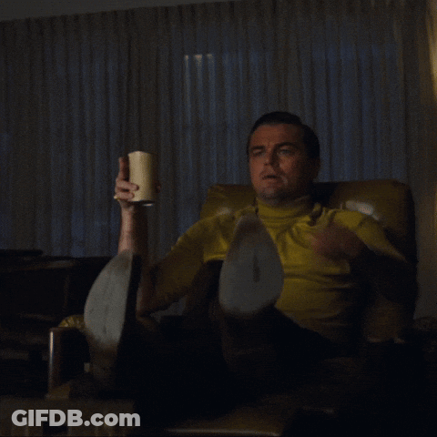 A Man In A Yellow Shirt Is Sitting In A Chair Pointing At Something GIF