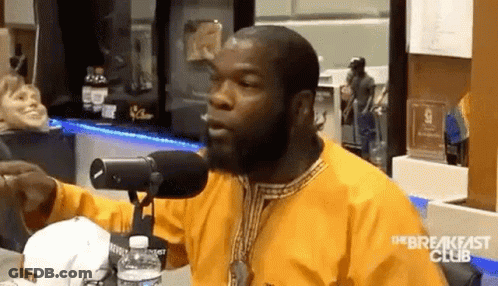 A Man In A Yellow Shirt Is Sitting In Front Of A Microphone And Talking Into It . GIF