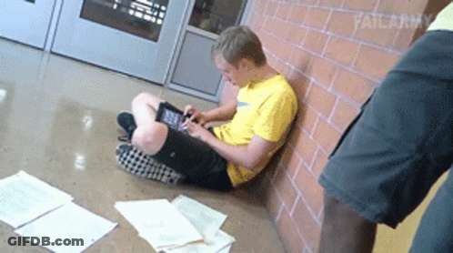 A Man In A Yellow Shirt Is Sitting On The Floor Using A Tablet Computer GIF