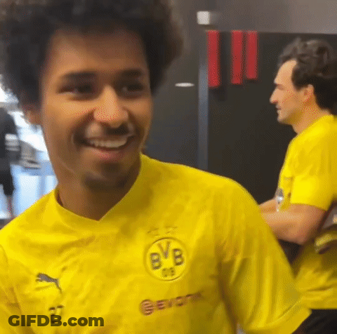 A Man In A Yellow Shirt Is Smiling In A Room . GIF