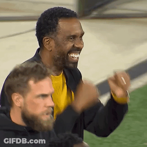 A Man In A Yellow Shirt Is Smiling While Another Man In A Black Jacket Looks On GIF