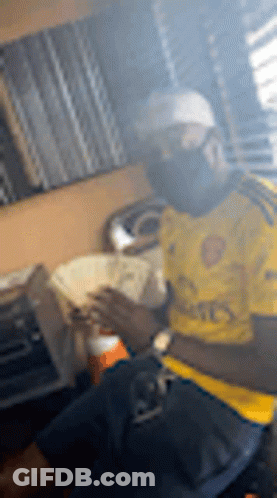 A Man In A Yellow Shirt Is Smoking A Cigarette While Holding A Bunch Of Money . GIF