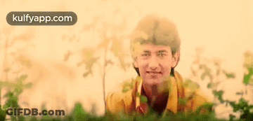 A Man In A Yellow Shirt Is Standing In A Field Of Grass . GIF