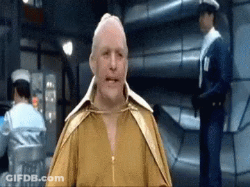 A Man In A Yellow Shirt Is Standing In A Room With A Police Officer Behind Him . GIF