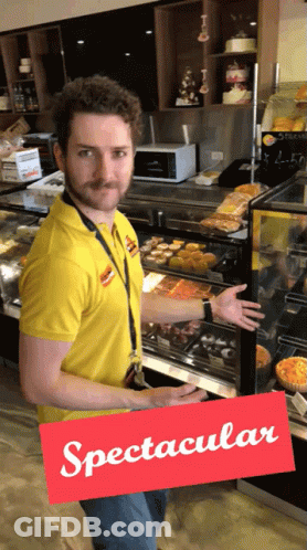 A Man In A Yellow Shirt Is Standing In Front Of A Display Case And A Sign That Says Spectacular GIF