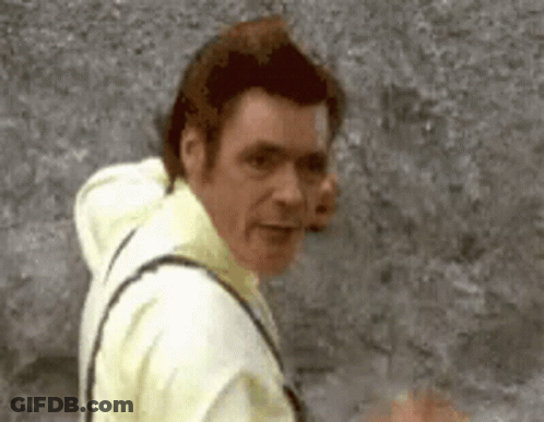 A Man In A Yellow Shirt Is Standing In Front Of A Gray Wall . GIF
