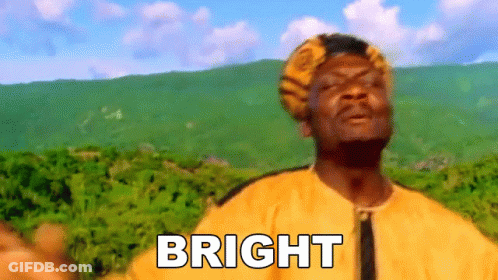 A Man In A Yellow Shirt Is Standing In Front Of A Mountain With The Word Bright Written On His Chest . GIF
