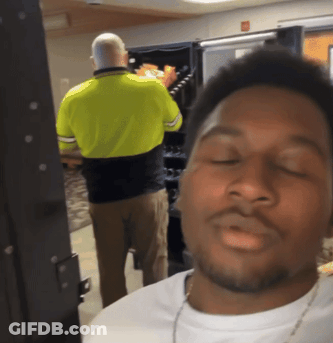 A Man In A Yellow Shirt Is Standing In Front Of A Vending Machine With His Eyes Closed GIF