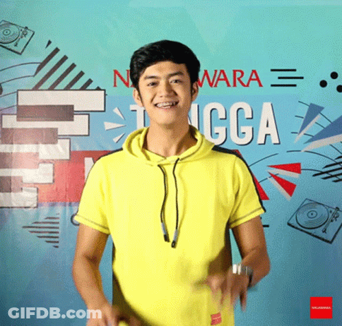 A Man In A Yellow Shirt Is Standing In Front Of A Wall That Says Nwara GIF