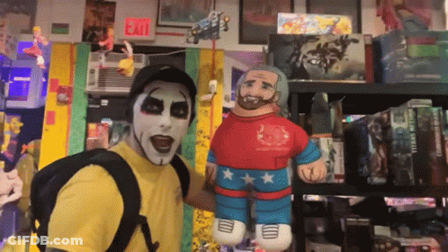 A Man In A Yellow Shirt Is Standing Next To A Stuffed Wrestler GIF