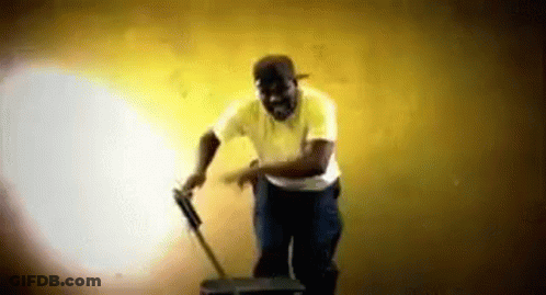 A Man In A Yellow Shirt Is Standing Next To A Suitcase And A Mop . GIF