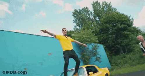 A Man In A Yellow Shirt Is Standing On A Car GIF