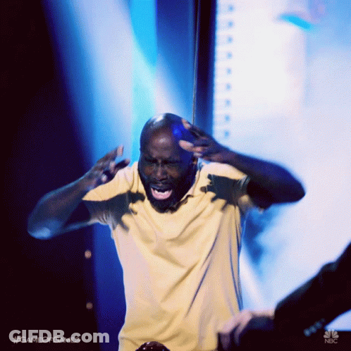 A Man In A Yellow Shirt Is Standing On A Stage With His Mouth Open GIF