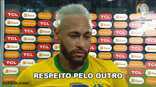 A Man In A Yellow Shirt Says " Respeito Pelo Outro " In Front Of A Wall Of Tcl Stickers GIF