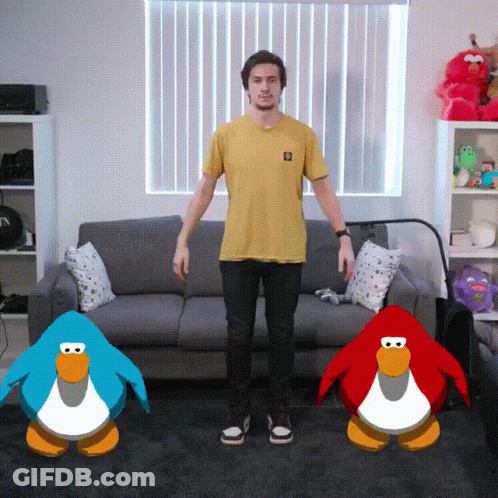 A Man In A Yellow Shirt Stands In Front Of A Couch And Two Penguins GIF