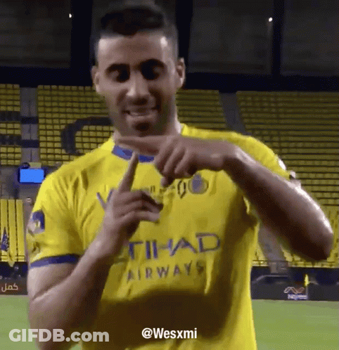 A Man In A Yellow Shirt That Says Etihad Airways Is Pointing GIF