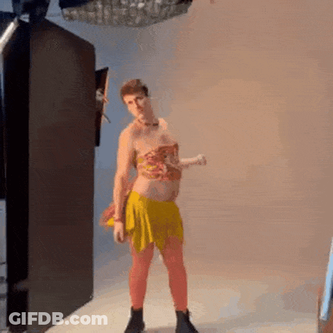 A Man In A Yellow Skirt And Top Is Standing In A Room . GIF