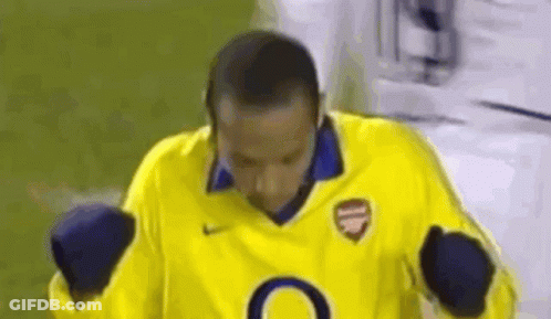 A Man In A Yellow Soccer Jersey Is Standing On A Field With His Hands In The Air . GIF